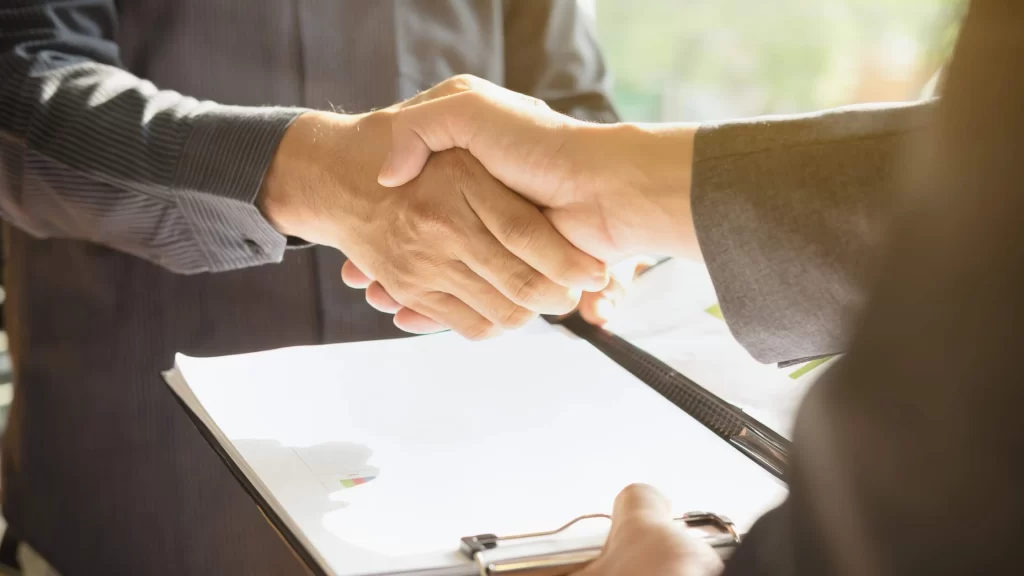 Two person shaking hand and one person is holding some documents in one hand