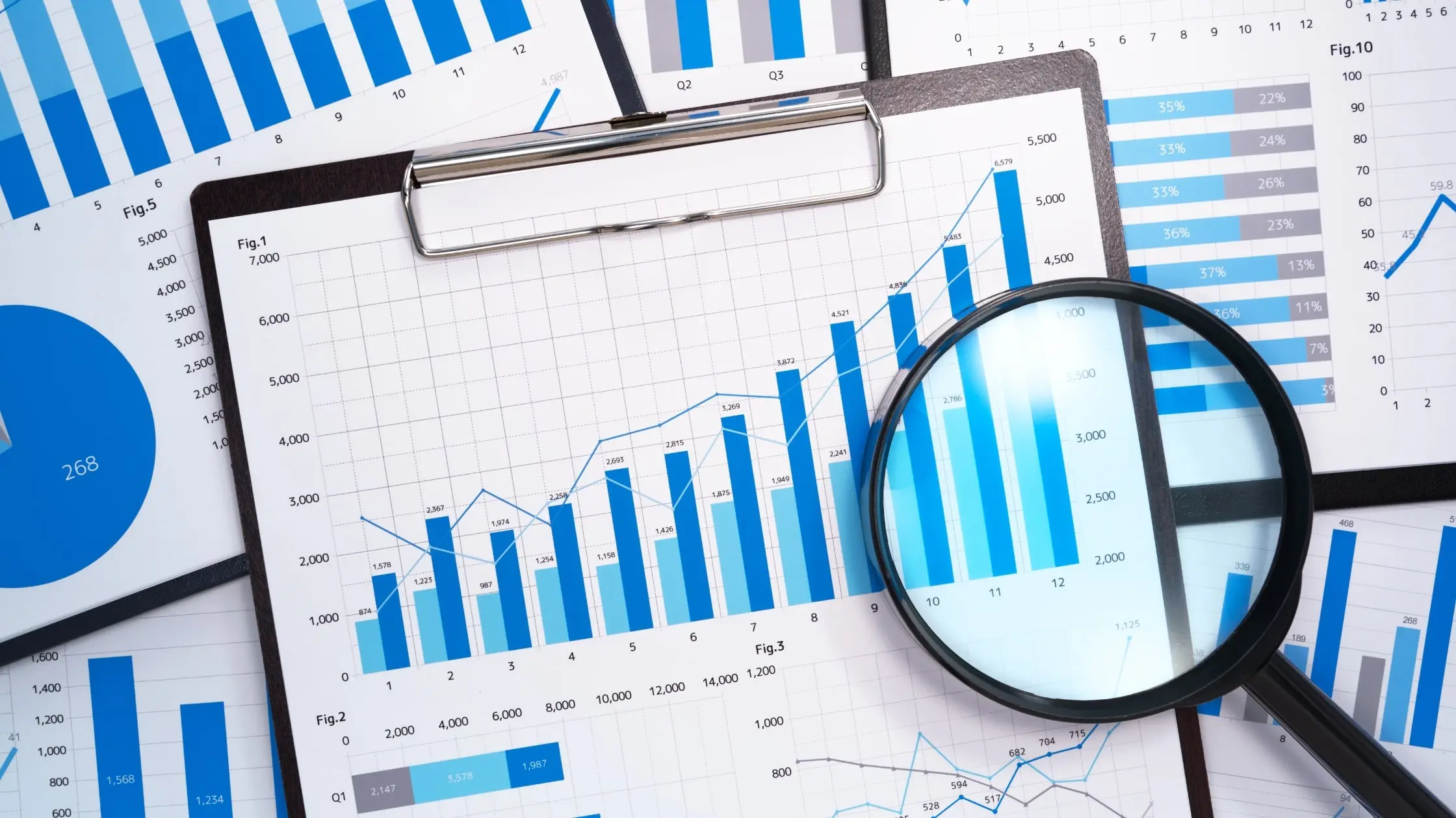 a clipboard with a sheet of paper showing data anaylitics growth focused by a magnifying glass